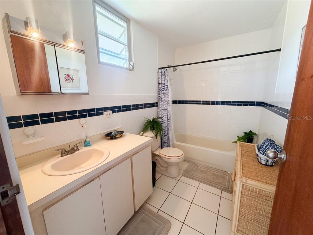 A bathroom features a white vanity, a tiled shower-tub combination, and a window — #16 COND. PARGUERA SUITES, LAJAS, PR
