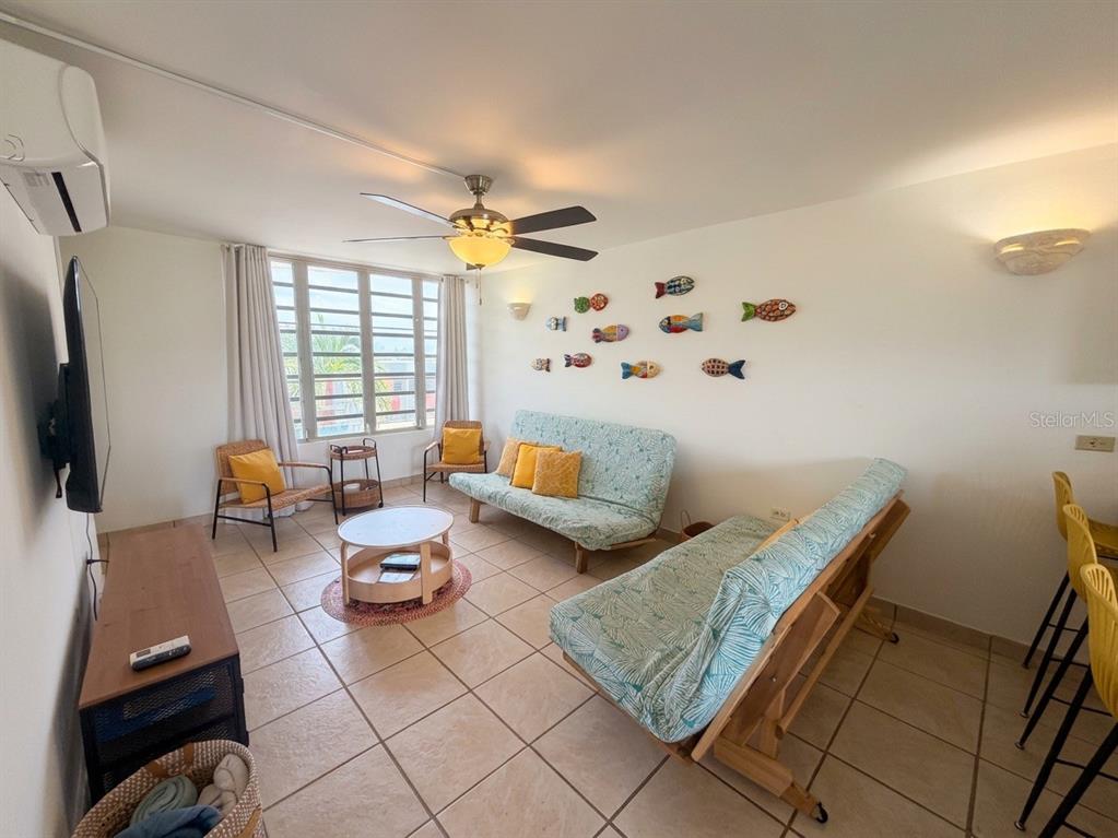 A living room features tile floors, two futons, wicker chairs, and decorative fish wall art — #16 COND. PARGUERA SUITES, LAJAS, PR