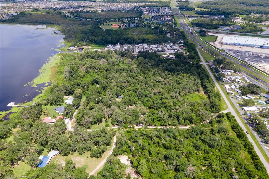 An aerial view shows a wooded lot bordering a lake next to a highway — 7476 NE 49TH LANE, WILDWOOD, FL