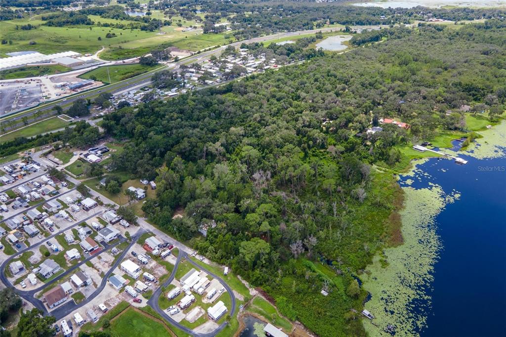 An aerial view shows a wooded lot situated between a residential community and a lake — 7476 NE 49TH LANE, WILDWOOD, FL