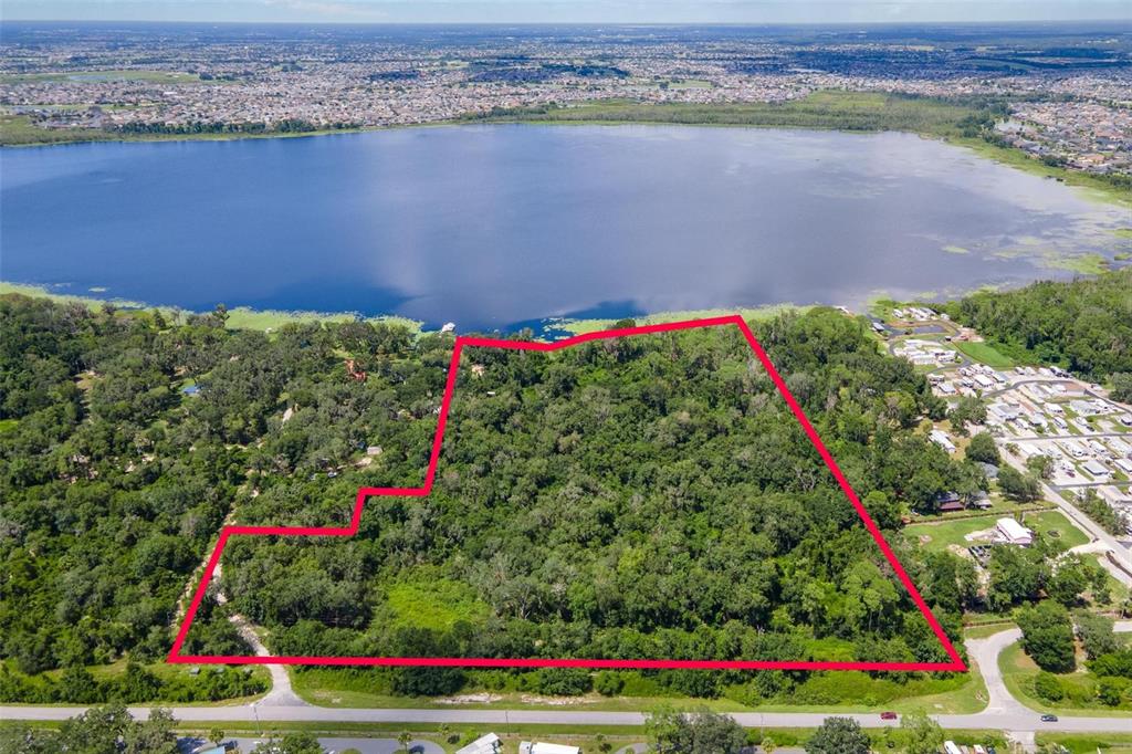 An aerial view shows a large, wooded plot of land outlined in red near a lake — 7476 NE 49TH LANE, WILDWOOD, FL
