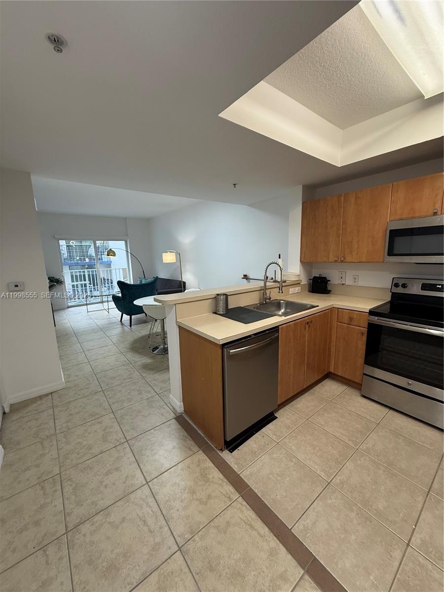 A kitchen with wood cabinets and stainless steel appliances overlooks a dining and living area — 119 SW 6th Ave # 405, Miami FL 33130, MIAMI, FL
