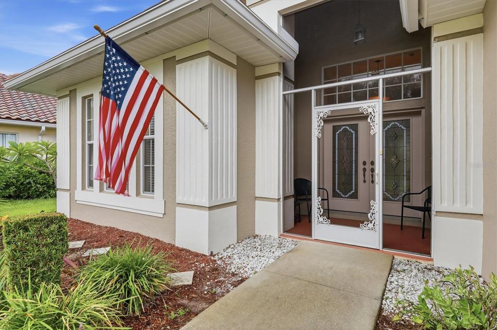 The exterior of a house features a front porch with a screen door and flag — 762 SILK OAK DRIVE, VENICE, FL