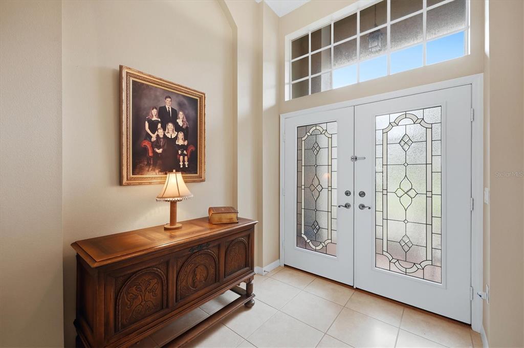An entryway features a wooden console table, a family portrait, and double glass-paneled front doors — 762 SILK OAK DRIVE, VENICE, FL