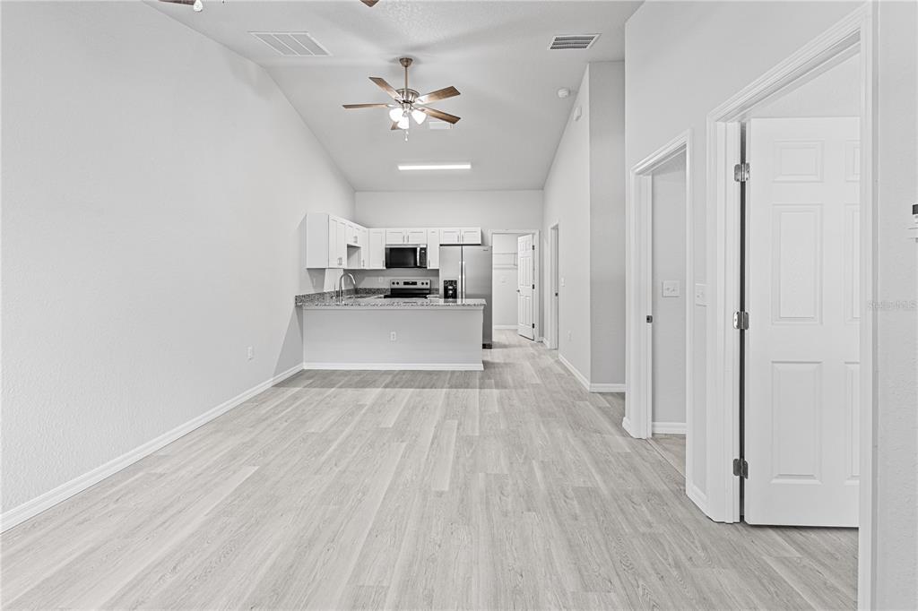 A bright, open-concept kitchen features white cabinetry, granite countertops, and light wood-look flooring — 607 SE 4TH DRIVE UNIT B, WILLISTON, FL