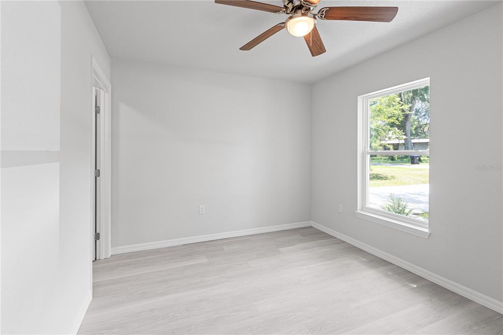 An empty bedroom features light gray walls, wood-look flooring, a ceiling fan, and a window — 607 SE 4TH DRIVE UNIT B, WILLISTON, FL