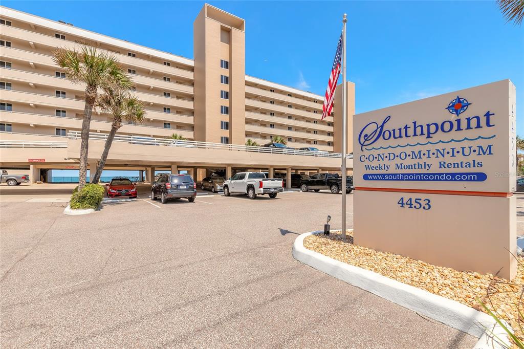 An exterior view of a multi-story condominium building with a parking garage and signage — 4453 S ATLANTIC AVENUE UNIT 703, PORT ORANGE, FL