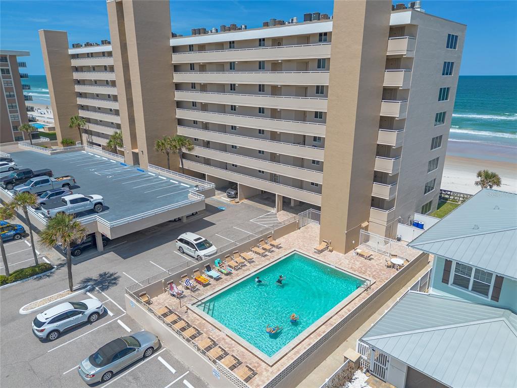 An aerial view shows a multi-story beachfront condominium building with a parking deck and pool — 4453 S ATLANTIC AVENUE UNIT 703, PORT ORANGE, FL