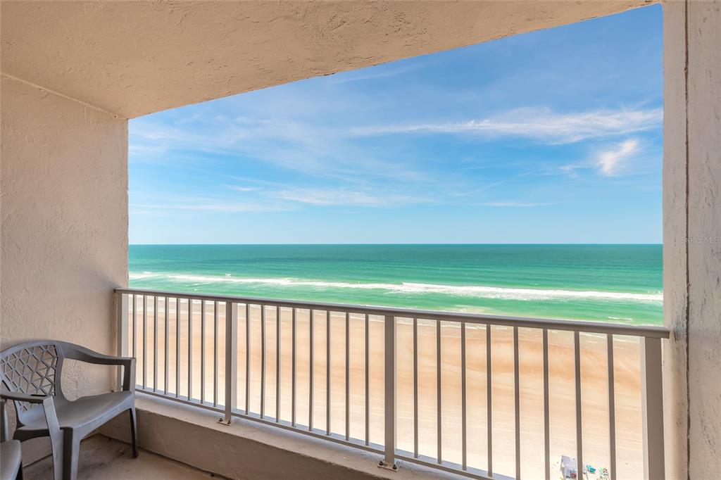 A balcony with a gray plastic chair overlooks a sandy beach and the ocean — 4453 S ATLANTIC AVENUE UNIT 703, PORT ORANGE, FL