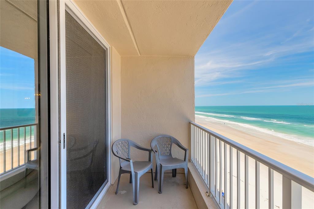 A balcony with two gray plastic chairs overlooks a sandy beach and the ocean — 4453 S ATLANTIC AVENUE UNIT 703, PORT ORANGE, FL
