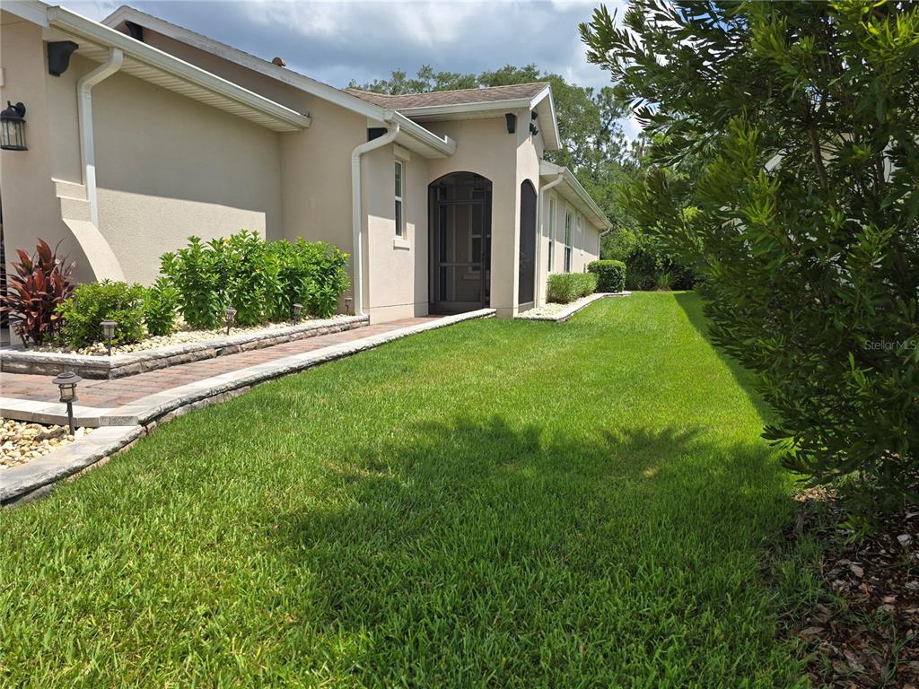 A paved walkway leads along the side of a beige house toward a screened entryway — 373 VESTRELLA DRIVE, POINCIANA, FL