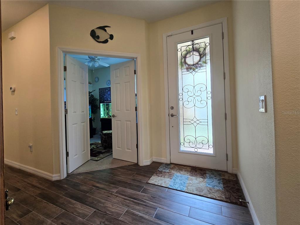 An entryway features wood-look tile flooring, a glass-paneled front door, and double doors leading inside — 373 VESTRELLA DRIVE, POINCIANA, FL