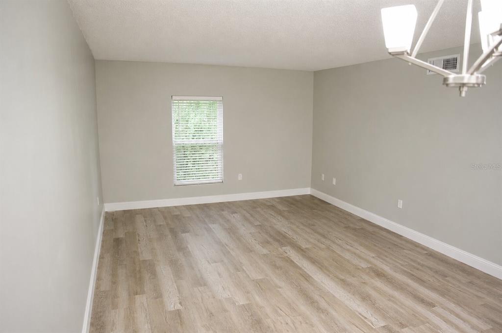 An empty room with light gray walls, wood-look flooring, and a modern chandelier — 165 PICARDY VILLA CIRCLE UNIT 201, BRANDON, FL