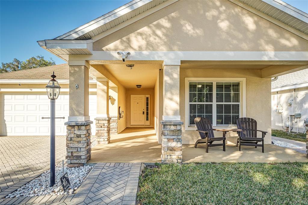 A covered front porch with stone pillars, two dark chairs, and a paved walkway — 7233 WAKEVIEW DRIVE, DAVENPORT, FL