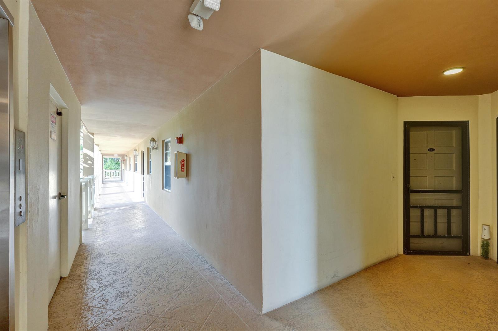 An outdoor apartment hallway features tiled floors, a fire extinguisher cabinet, and a screen door — 304 Golfview Road # 304, North Palm Beach FL 33408, NORTH PALM BEACH, FL