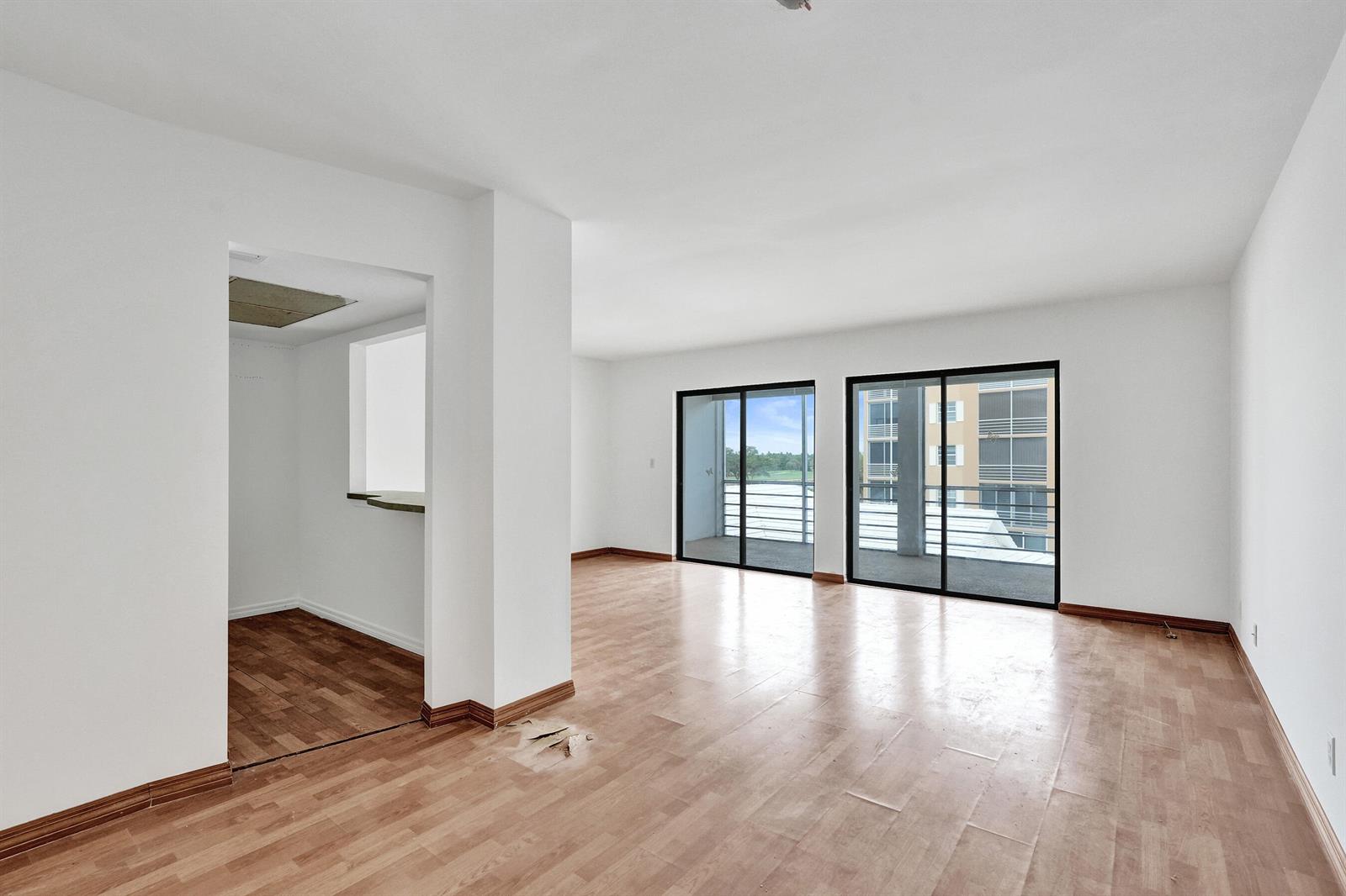 An empty room features light wood-look flooring, white walls, and two sliding glass balcony doors — 304 Golfview Road # 304, North Palm Beach FL 33408, NORTH PALM BEACH, FL