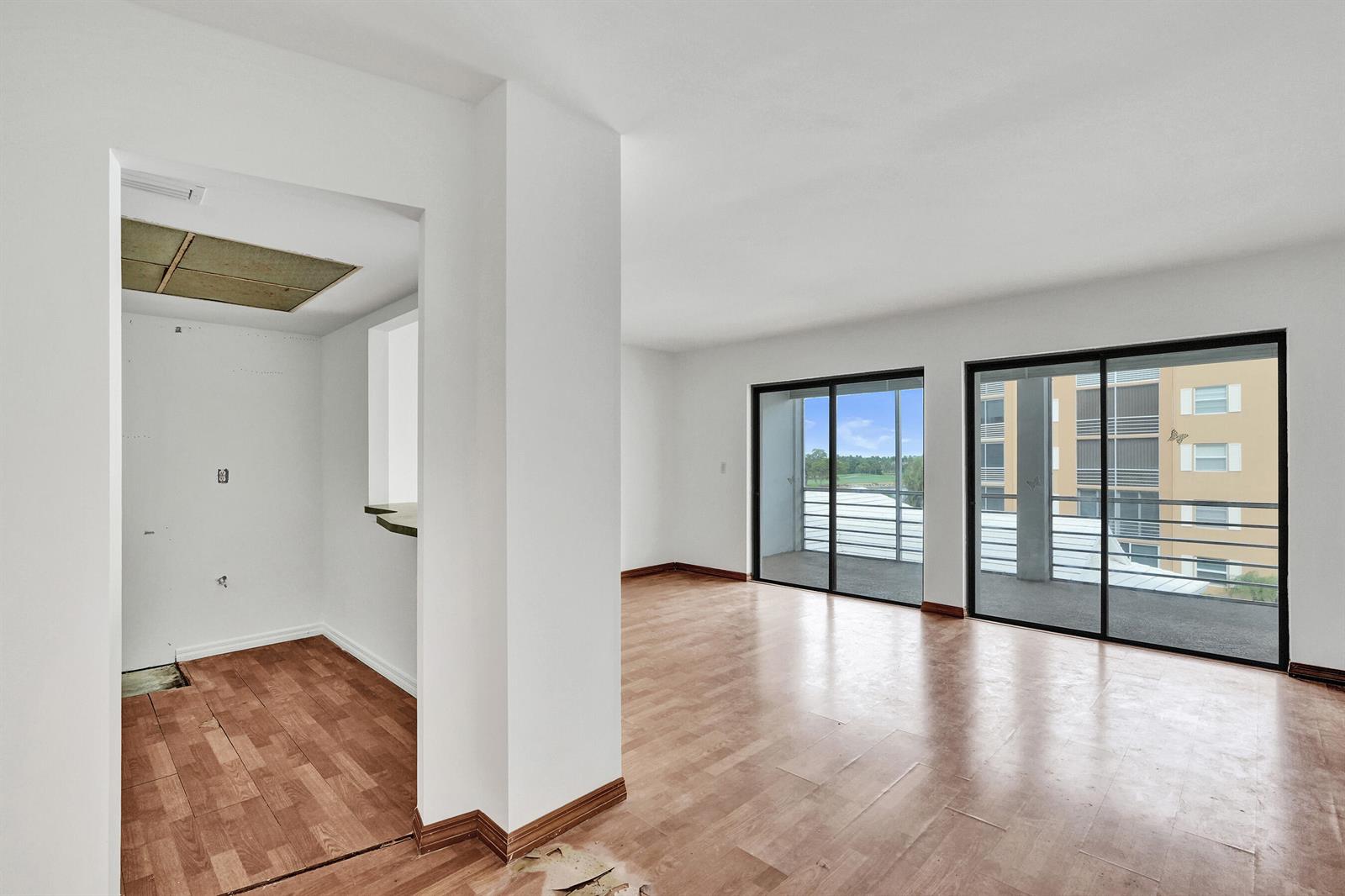 An empty living room with wood-look flooring and two sliding glass doors leading to balconies — 304 Golfview Road # 304, North Palm Beach FL 33408, NORTH PALM BEACH, FL