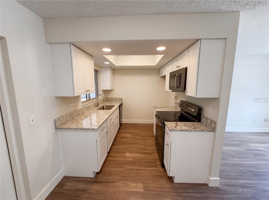 A galley kitchen features white cabinets, granite countertops, and wood-look flooring — 2768 GALATIAN PLACE, ORLANDO, FL