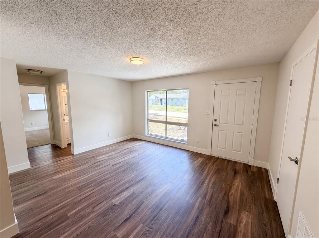 A living room with wood-look flooring, a large window, and a white front door — 2768 GALATIAN PLACE, ORLANDO, FL