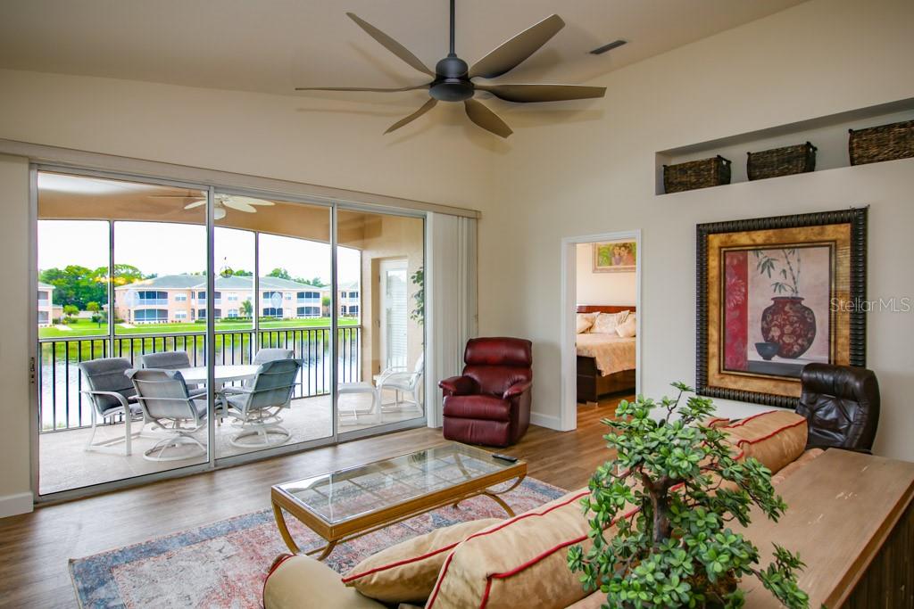 A living room with a ceiling fan, sliding glass doors to a balcony, and wood flooring — 6448 7TH AVENUE CIRCLE W, BRADENTON, FL