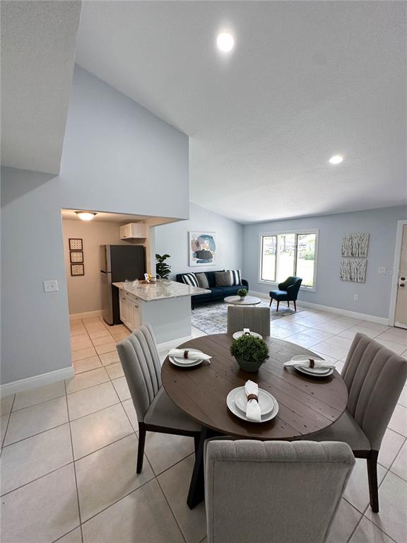 A dining area with a round wooden table sits in front of an open kitchen and living room — 23 COUNTRY CLUB DRIVE UNIT B, NEW SMYRNA BEACH, FL