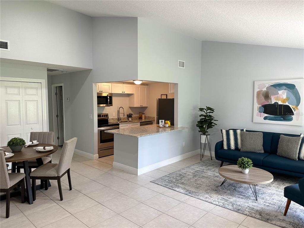 An open-concept living and dining area features a kitchen with granite countertops and white cabinets — 23 COUNTRY CLUB DRIVE UNIT B, NEW SMYRNA BEACH, FL