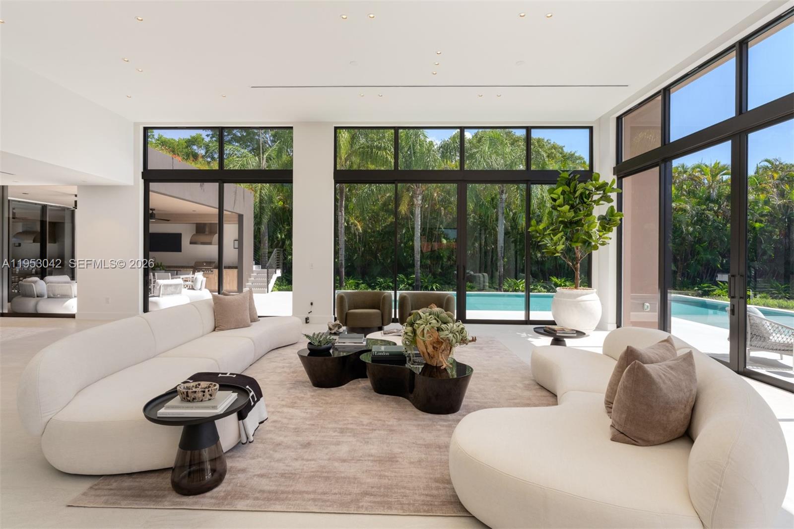 A modern living room features white curved sofas, black coffee tables, and large floor-to-ceiling windows — 5825 SW 111th Ter, Pinecrest FL 33156, PINECREST, FL