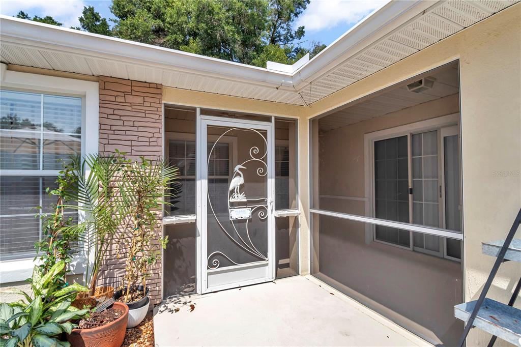A covered entryway features a screen door with a heron design and a stone-accented wall — 7229 SW 115TH PLACE, OCALA, FL