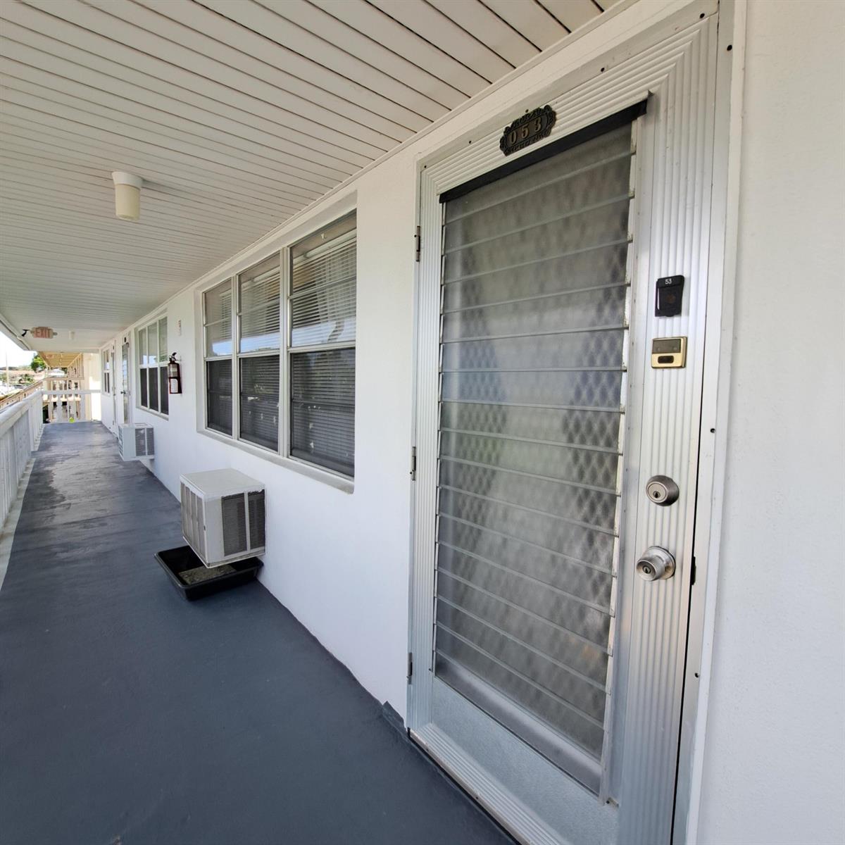 An exterior walkway leads to a unit door with a louvered glass window and air conditioner — 53 Northampton C, West Palm Beach FL 33417, WEST PALM BEACH, FL