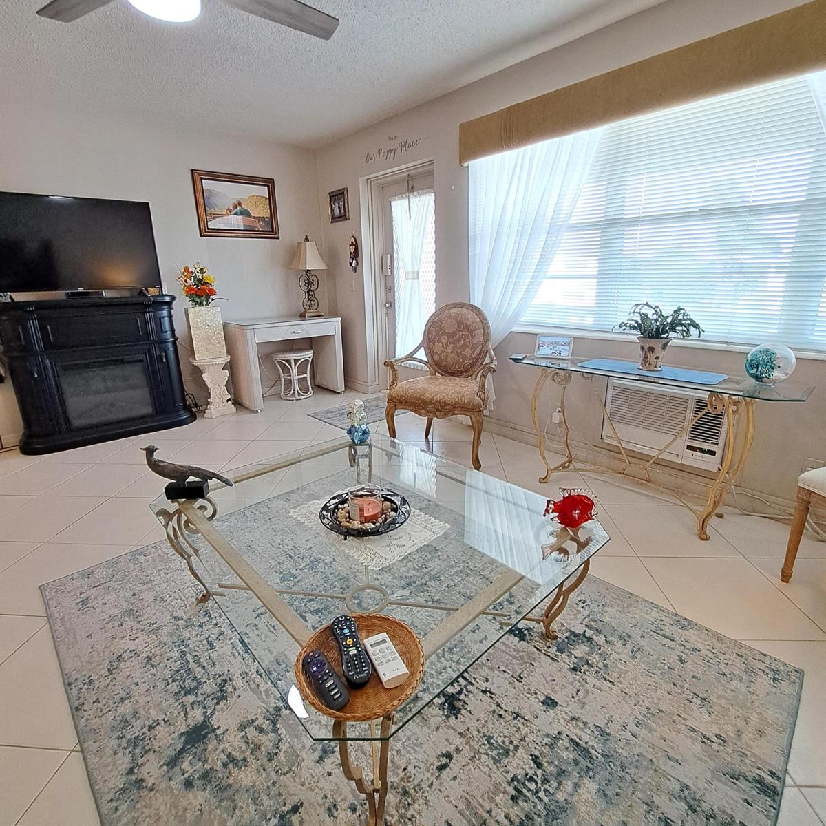 A living room features a glass coffee table, a fireplace, and a window with blinds — 53 Northampton C, West Palm Beach FL 33417, WEST PALM BEACH, FL