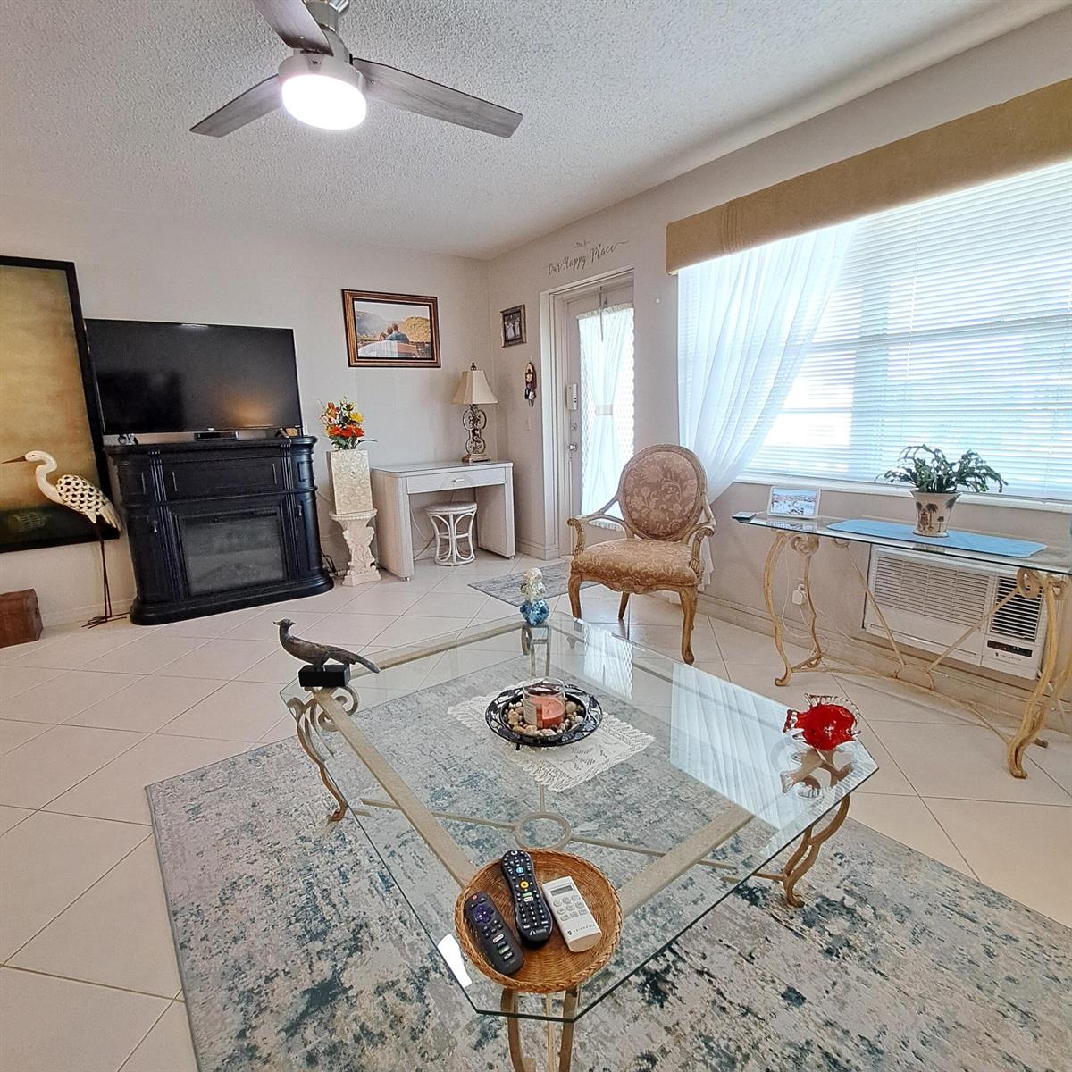 A living room features tile flooring, a glass coffee table, and a black fireplace console — 53 Northampton C, West Palm Beach FL 33417, WEST PALM BEACH, FL