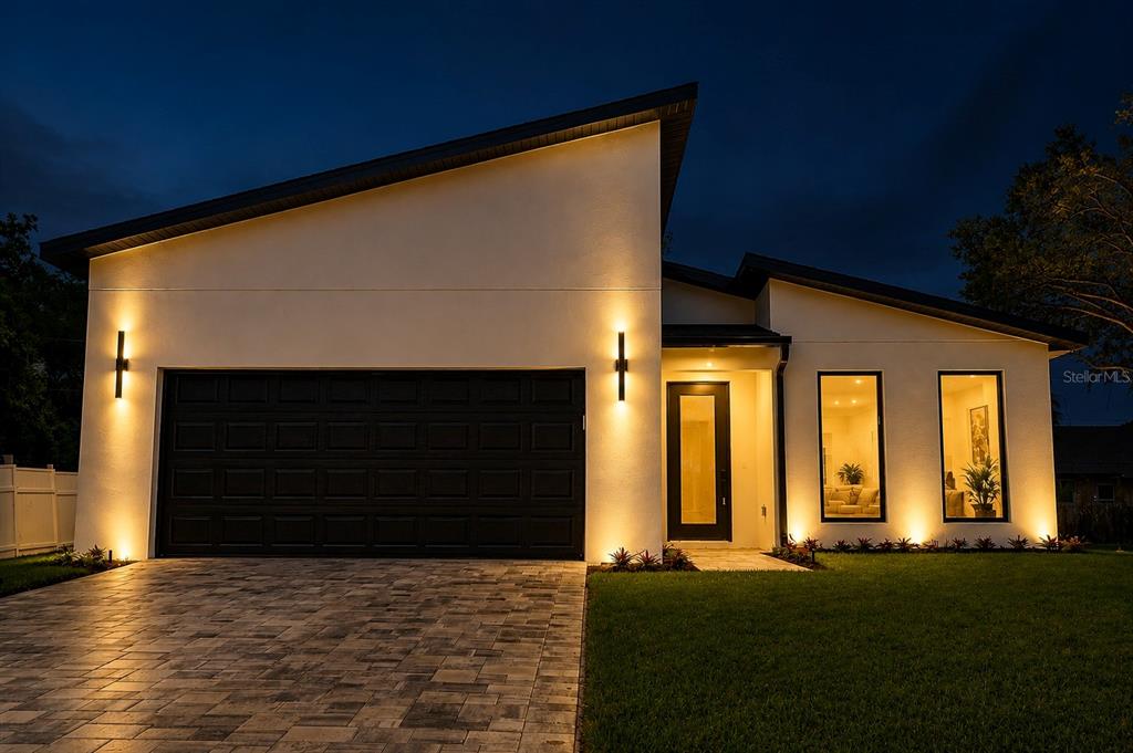 A modern, single-story house exterior at night with a paved driveway and illuminated wall sconces — 301 EPPINGER DRIVE, PORT CHARLOTTE, FL