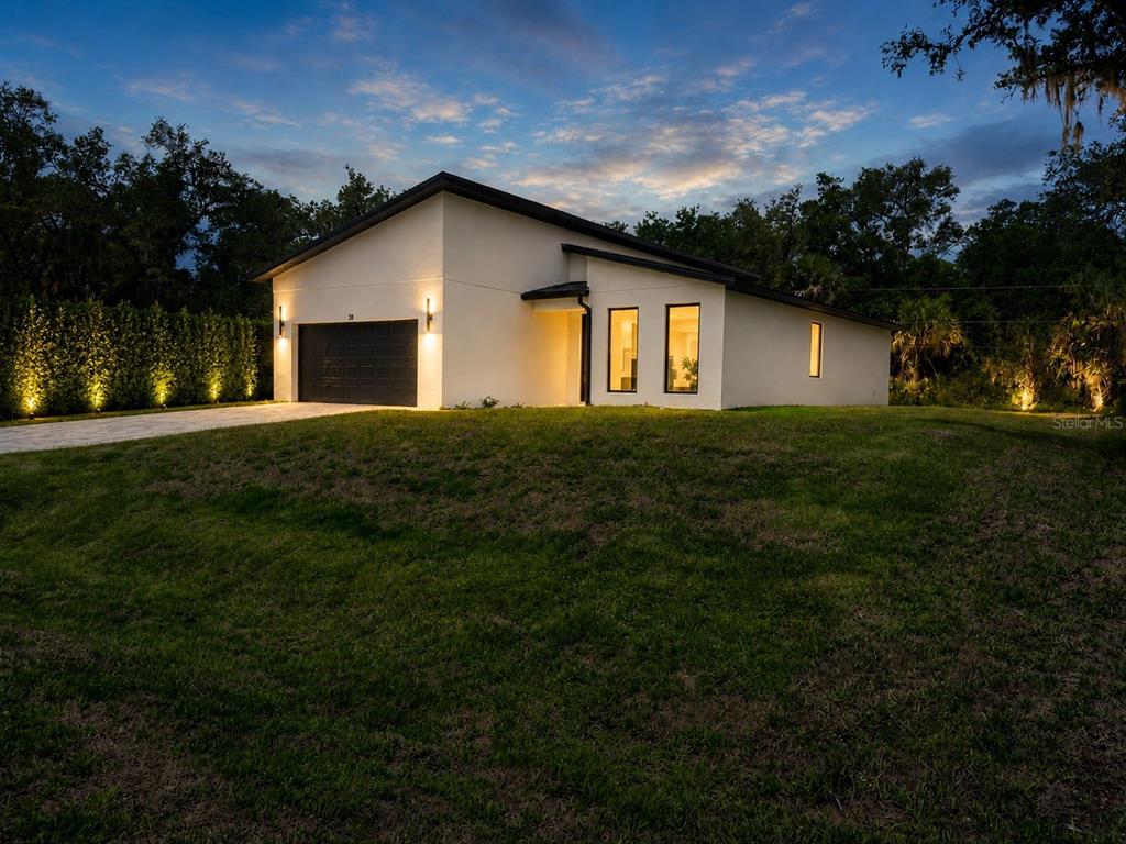 A modern white house with a black garage door and roof sits on a grassy lot — 301 EPPINGER DRIVE, PORT CHARLOTTE, FL