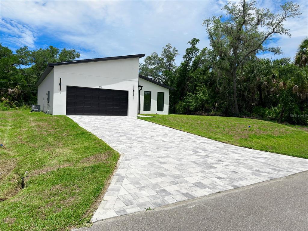 A modern white house with a black garage door and a paved driveway — 301 EPPINGER DRIVE, PORT CHARLOTTE, FL
