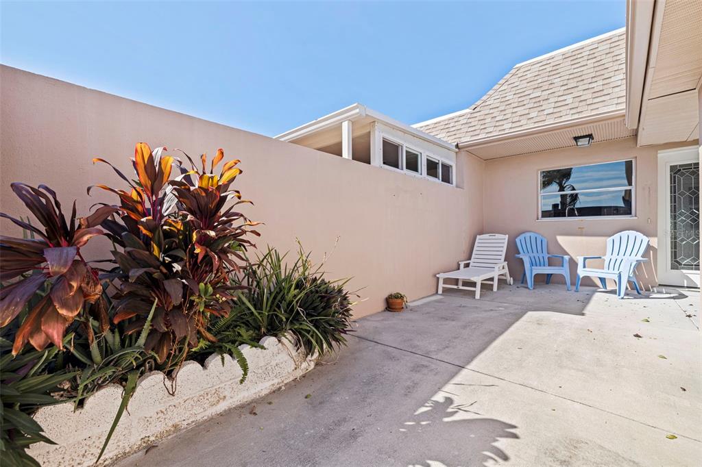 A concrete patio features a garden bed, three chairs, and a light-colored privacy wall — 409 BOCA CIEGA POINT BOULEVARD S UNIT 409, ST PETERSBURG, FL