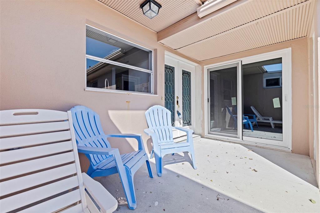 A covered patio features a concrete floor, three plastic chairs, and sliding glass doors — 409 BOCA CIEGA POINT BOULEVARD S UNIT 409, ST PETERSBURG, FL