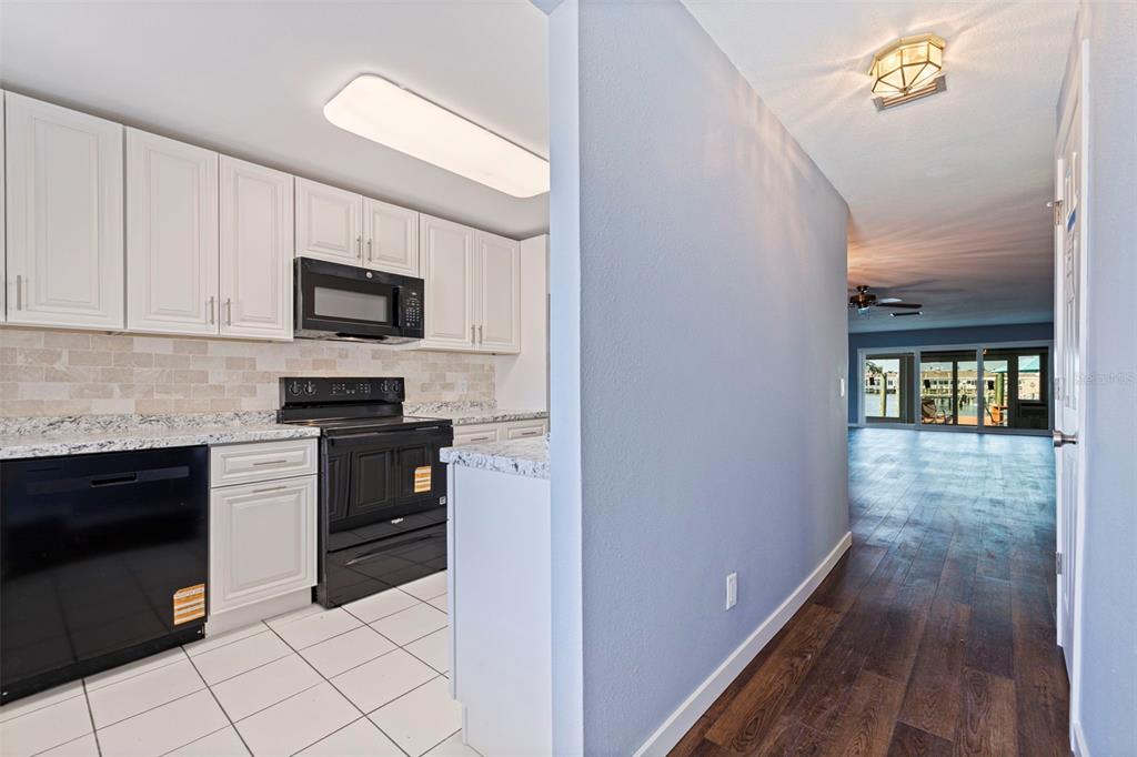 A kitchen with white cabinets and black appliances opens to a hallway with wood flooring — 409 BOCA CIEGA POINT BOULEVARD S UNIT 409, ST PETERSBURG, FL