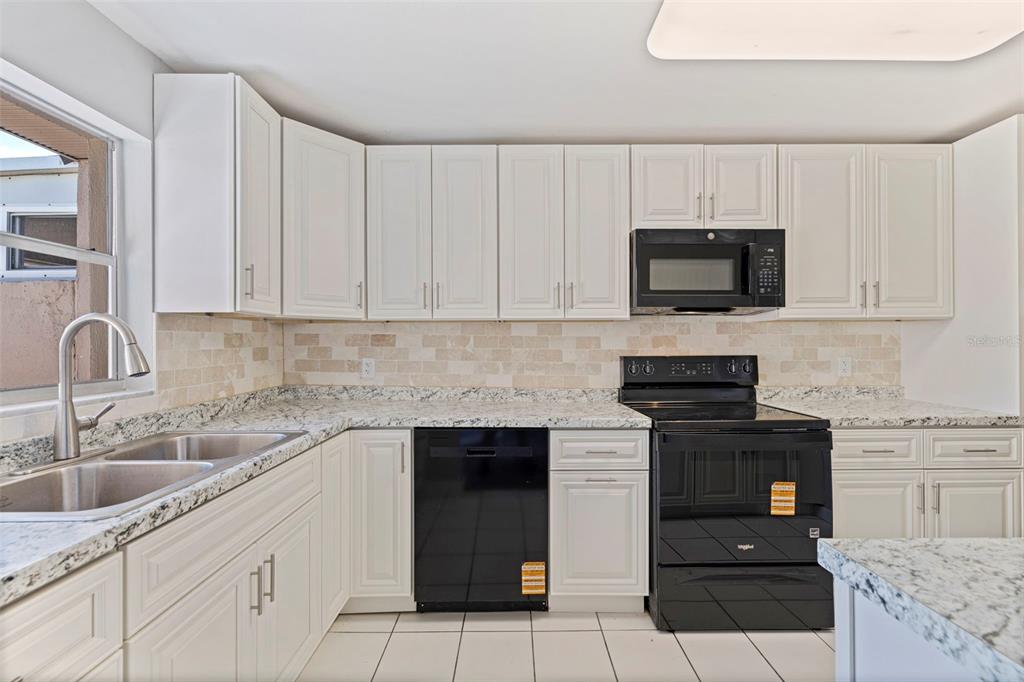 A kitchen features white cabinets, granite countertops, a tiled backsplash, and black appliances — 409 BOCA CIEGA POINT BOULEVARD S UNIT 409, ST PETERSBURG, FL