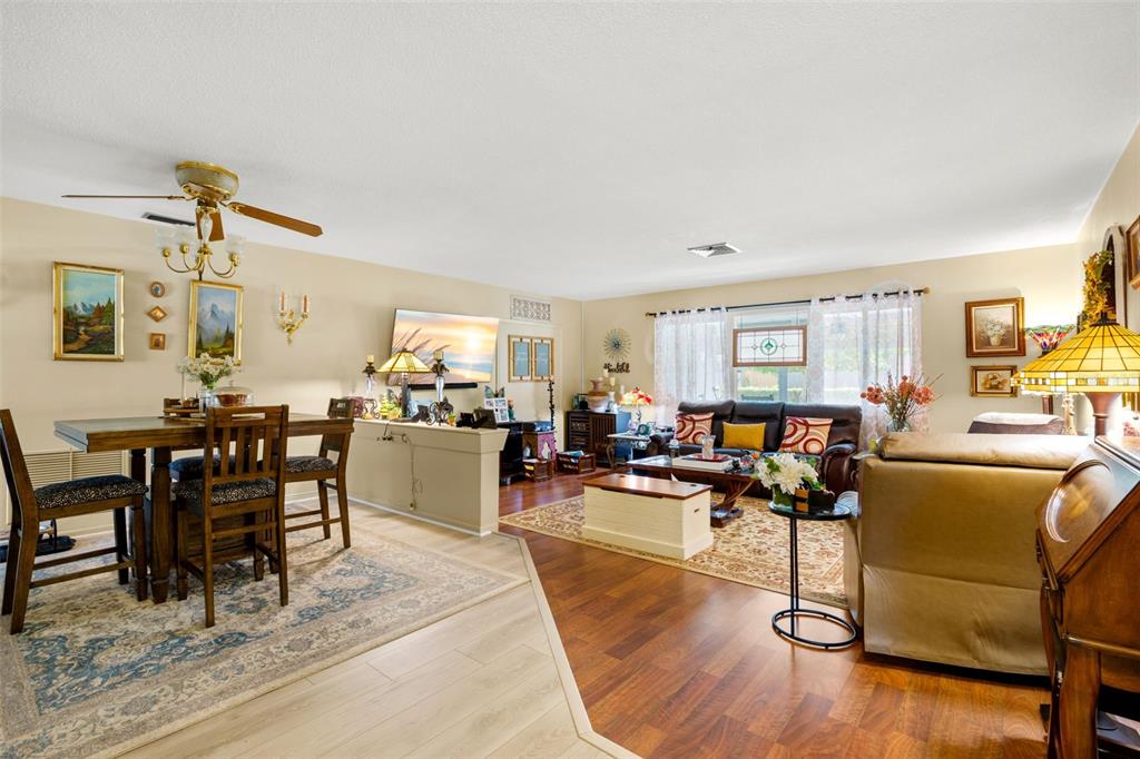 An open-concept living and dining area features wood-look flooring, a ceiling fan, and neutral walls — 29861 69TH STREET N, CLEARWATER, FL