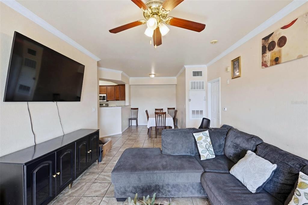 A living room features gray walls, tile flooring, a sofa, a television, and a balcony — 5526 PGA BOULEVARD UNIT 4927, ORLANDO, FL