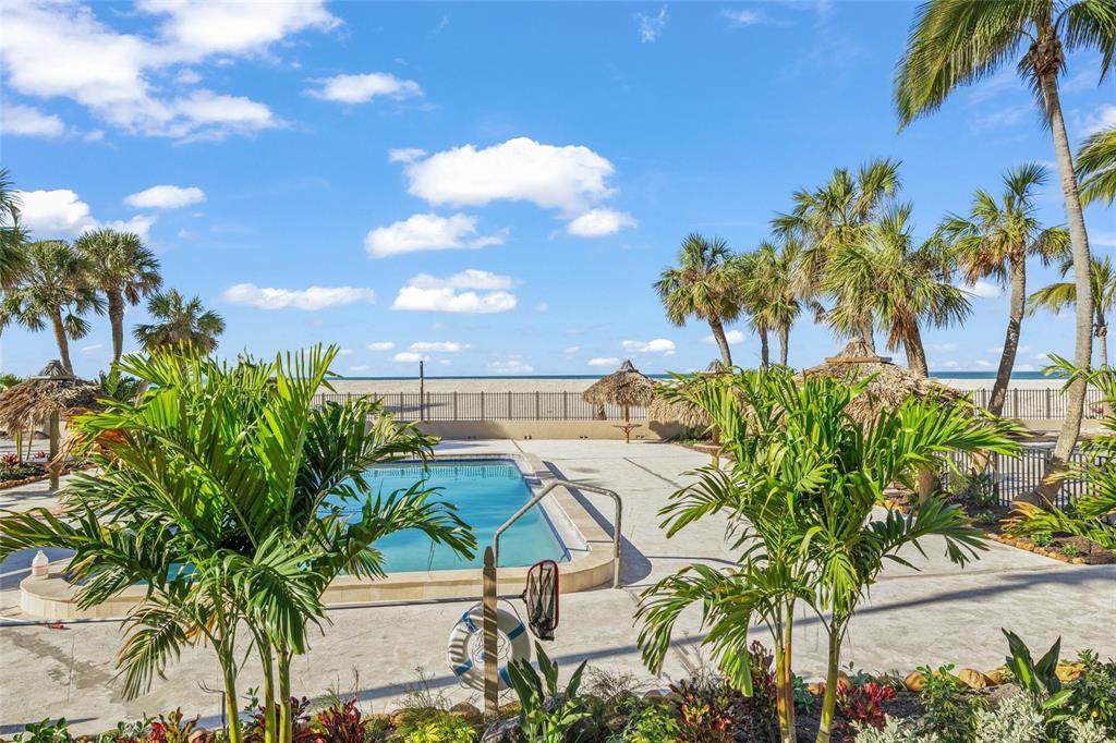 A swimming pool sits on a patio surrounded by palm trees with an ocean view — 1212 BENJAMIN FRANKLIN DRIVE UNIT 102, SARASOTA, FL