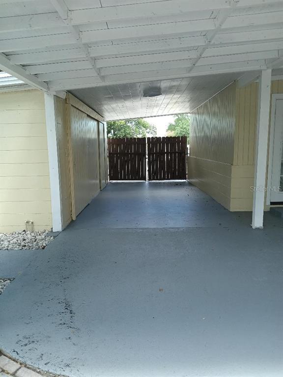 A covered carport features a concrete floor, light-colored walls, and a wooden privacy fence — 5700 CORTEZ DRIVE, ORLANDO, FL