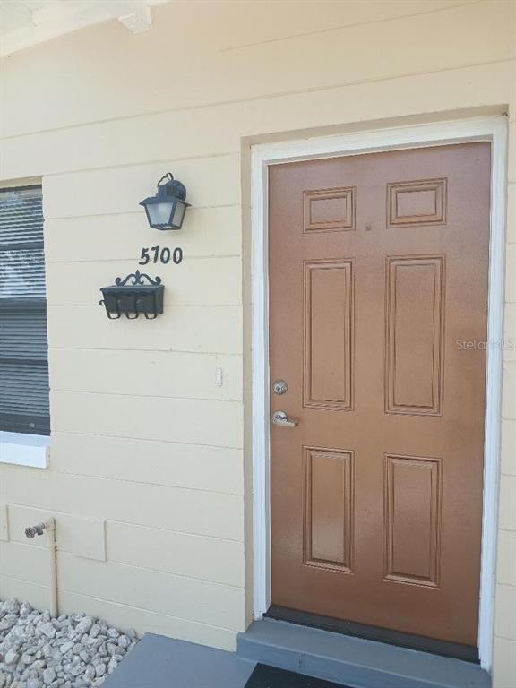 A tan exterior wall features a brown door, a black light fixture, and house numbers — 5700 CORTEZ DRIVE, ORLANDO, FL