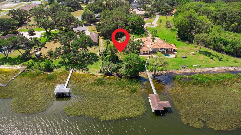 An aerial view shows a waterfront property with two docks, a house, and dense trees — 713 NEWELL HILL ROAD, LEESBURG, FL