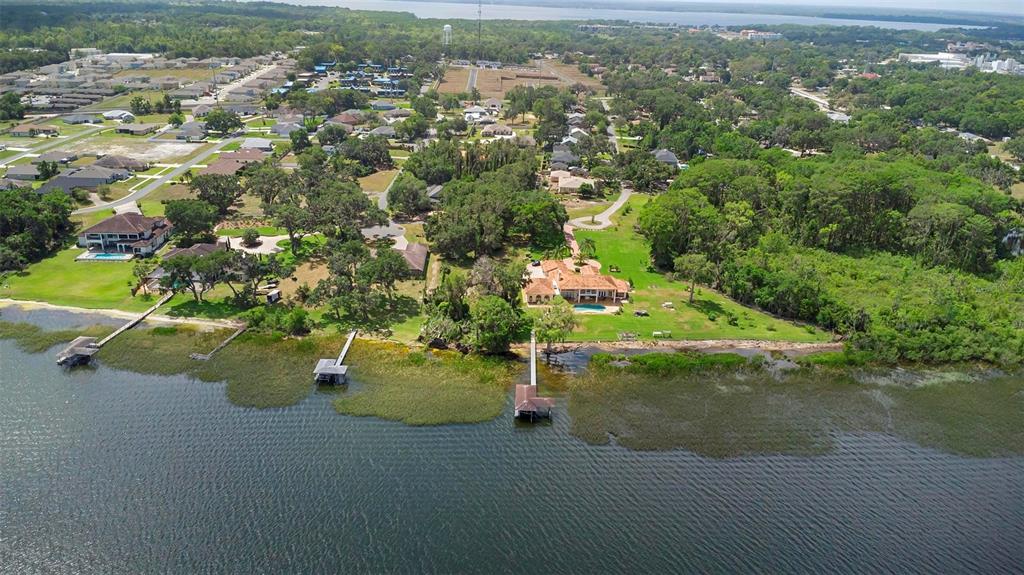 An aerial view shows waterfront homes with private docks along a tree-lined lake shore — 713 NEWELL HILL ROAD, LEESBURG, FL