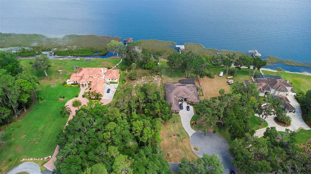 An aerial view shows three large houses situated on a grassy waterfront lot with trees — 713 NEWELL HILL ROAD, LEESBURG, FL