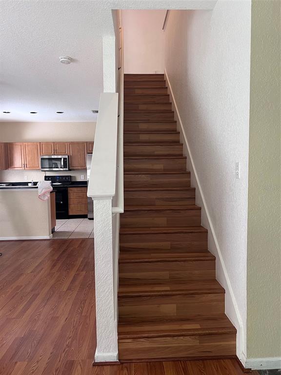 A staircase with wood-look treads leads upward next to a kitchen with wooden cabinets — 16317 NEWBURY PALMS COURT, TAMPA, FL