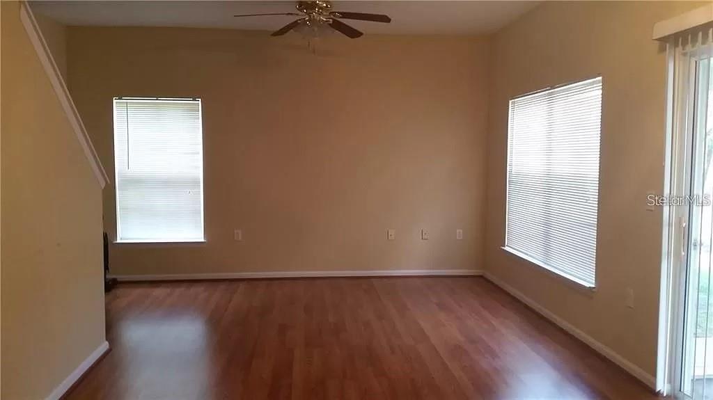 An empty room features wood-look flooring, beige walls, two windows with blinds, and a ceiling fan — 16317 NEWBURY PALMS COURT, TAMPA, FL