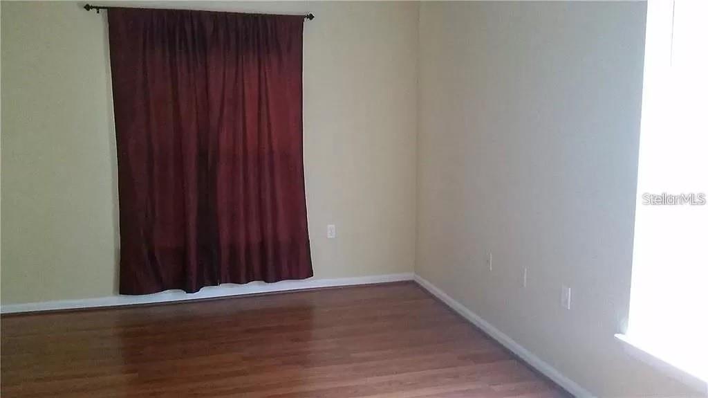 An empty room with hardwood floors, beige walls, and dark curtains over a window — 16317 NEWBURY PALMS COURT, TAMPA, FL