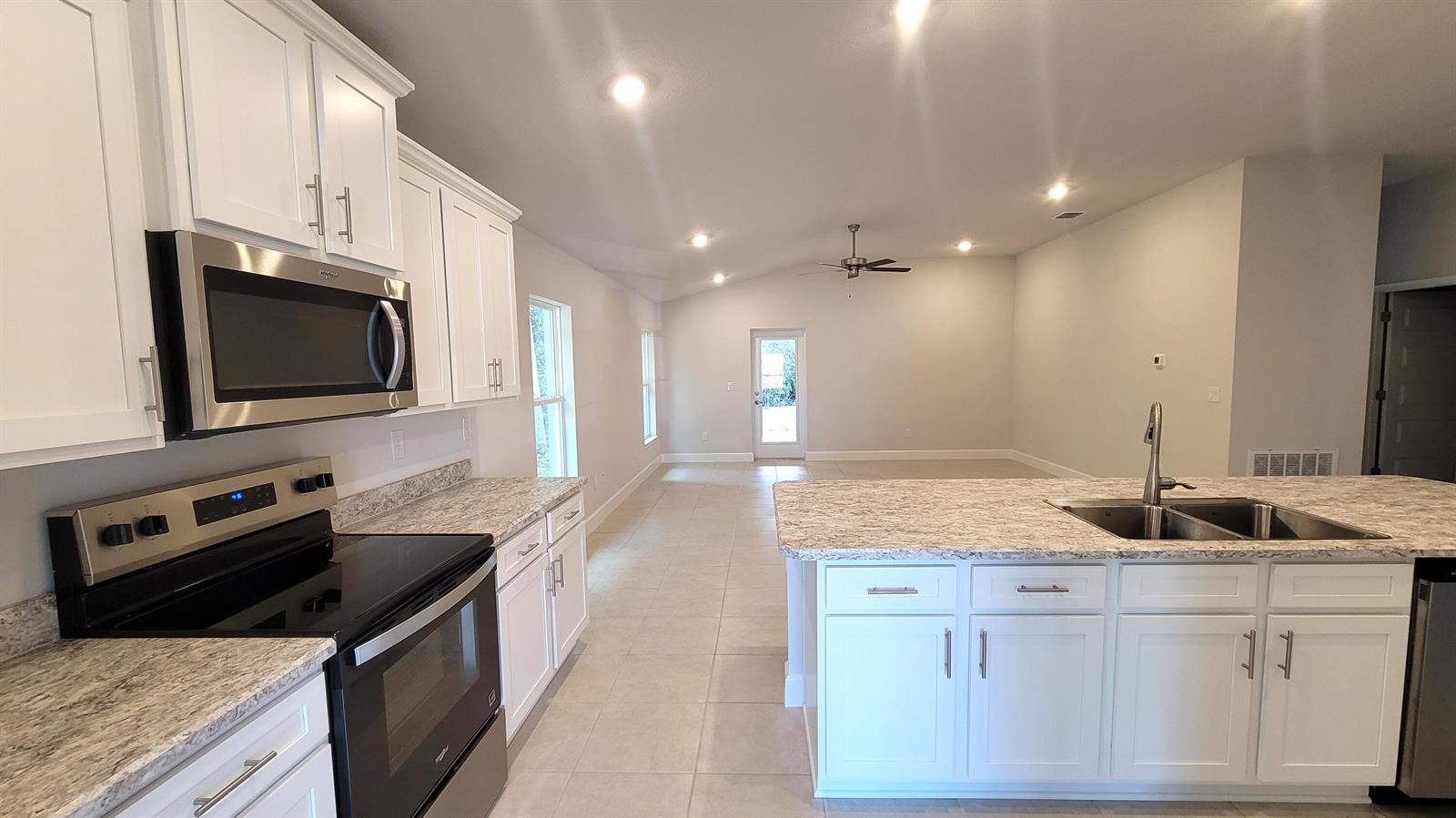 A kitchen with white cabinets, granite countertops, and stainless steel appliances opens to a living area — 8844 Waterstone Boulevard, Fort Pierce FL 34951, FORT PIERCE, FL